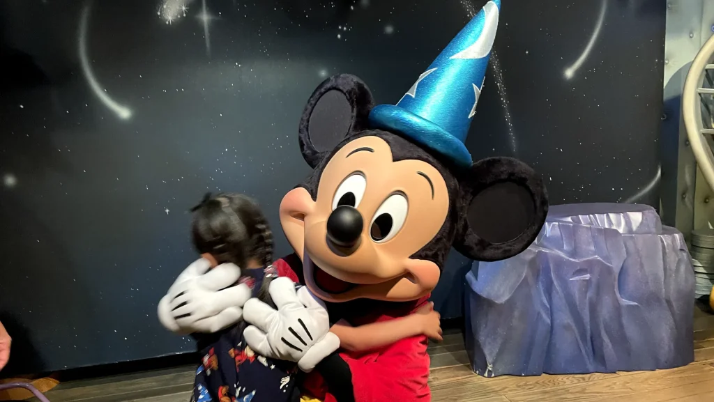 「ミッキーの家とミート・ミッキー」で、魔法使いの帽子をかぶったミッキーとハグする子ども