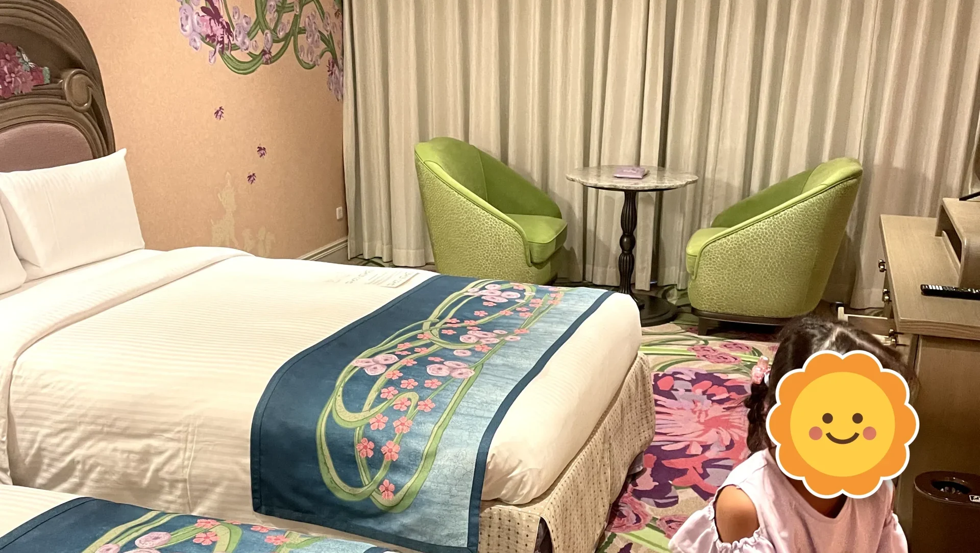 ファンタジースプリングスホテル「ファンタジーシャトー」の客室。花柄のベッドスローと緑のソファーがあり、手前に子どもがいる