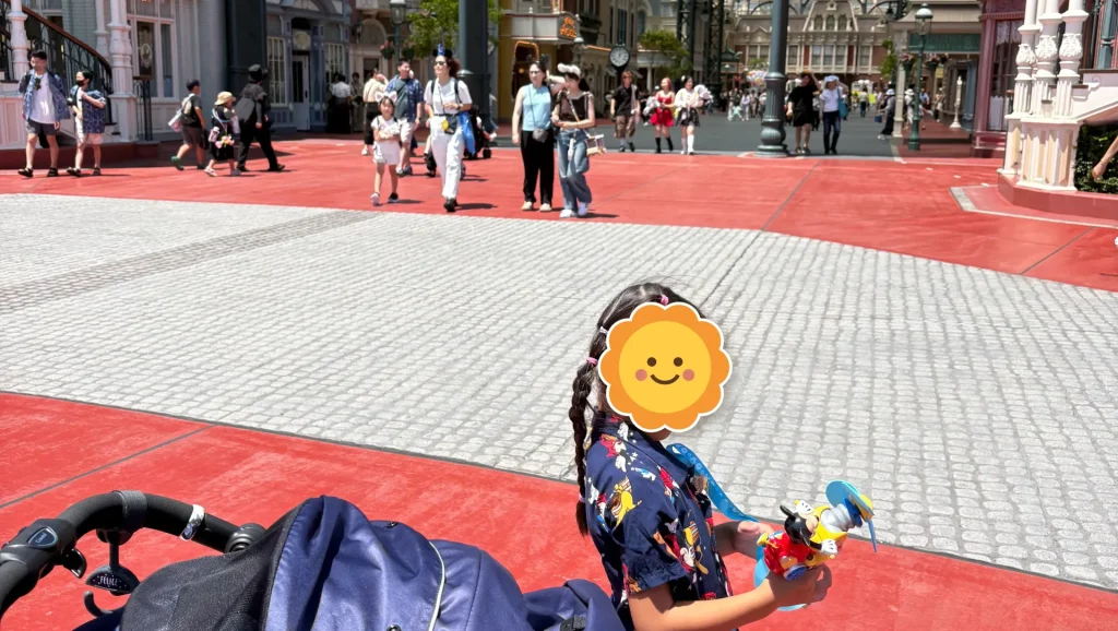 東京ディズニーランドのパーク内で、ミッキーのグッズを持ってベビーカーの横を歩く子ども